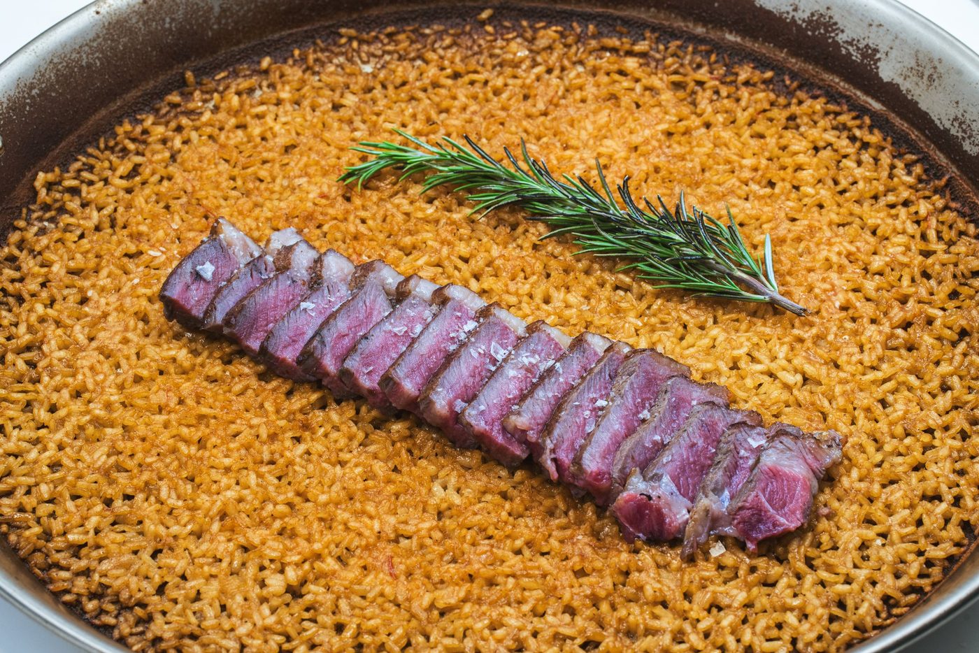 Sliced beef over saffron rice in the paella pan